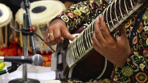 A classical music artist holding a sitar in his hand 