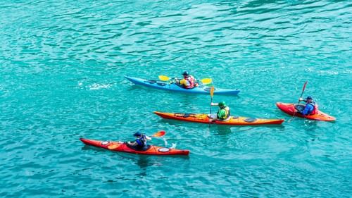 an images showing a group of four people kayaking in blue azure waters 