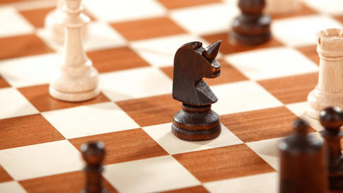 Black knight piece surrounded by white and black chess pieces on a wooden chessboard in a strategic mid-game position.