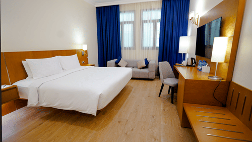 an overview of a room with a king bed and wall mounted tv opposite it - La Maison Hotel, Doha