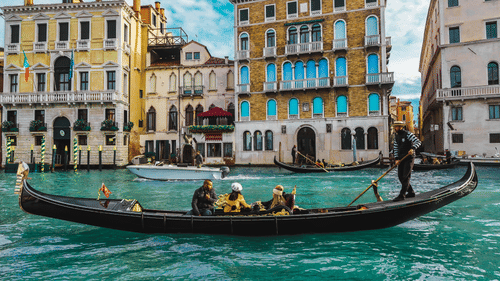 An overview of a gondola on a waterbody with people sitting and building in the background in view.