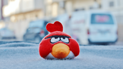 A close up of a plush toy of the game Angry Birds placed on a cloth and a car in the background.