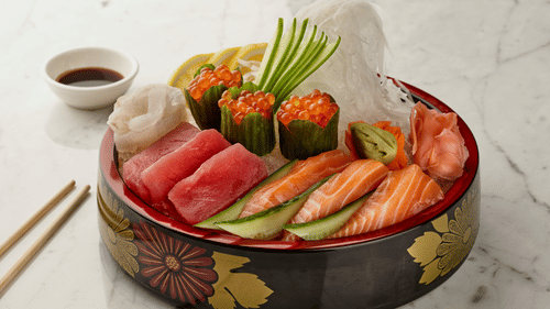 A variety of sashimi and sushi on a decorative platter, including tuna and salmon, with chopsticks and a small bowl of soy sauce on the side.