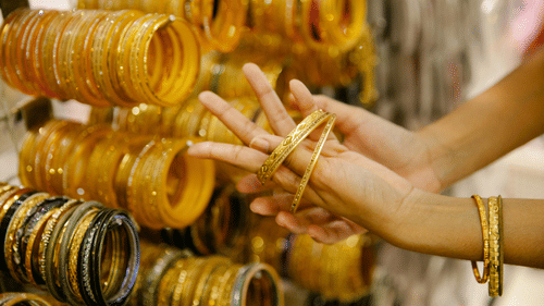 A person's hands are shown trying on multiple gold-coloured bangles from a large collection hanging on a stand.