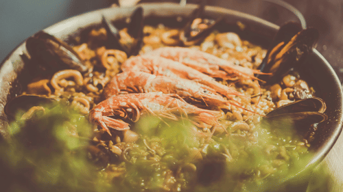 A close-up of a pot of seafood stew with prawns, mussels, and crabs. The dish has a green, foamy sauce.