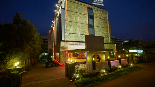 The MGM Mark Whitefield Business Hotel in Bengaluru glows warmly at night, a modern structure with red accents and inviting lights.