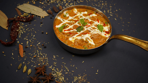 A curry placed in a bowl garnished with mint placed on a tale with spices around.