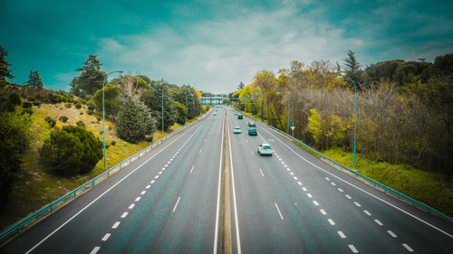 Shot of a highway with few cars running and trees on either side.