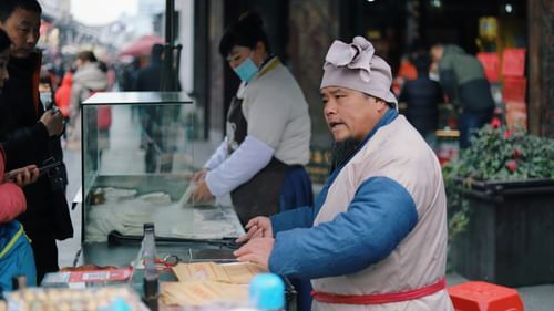 a local street vendor looking at a crowd while they order food from his cart
