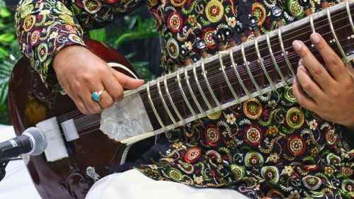 A person's hands wearing a turquoise ring on the fretboard of a sitar.