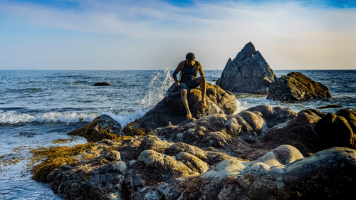 An overview of a person sitting on a rock along the coast of Cabo De Rama Beach.