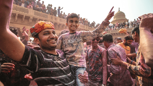 A close up of a father holding his son and dancing with many people looking from the building behind.