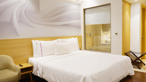 Deluxe room at Nemesia with a king size bed, modern decor, and a stylish en-suite bathroom visible through a glass partition.