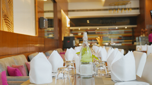 Dining table at Nemesia set with elegant white linens, glassware, and a refreshing beverage bottle, showcasing a refined dining experience.