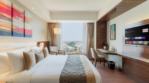 A bedroom at Nirvana Sarovar Portico, Gorakhpur featuring a king size bed, a study desk, a television, and a large window.