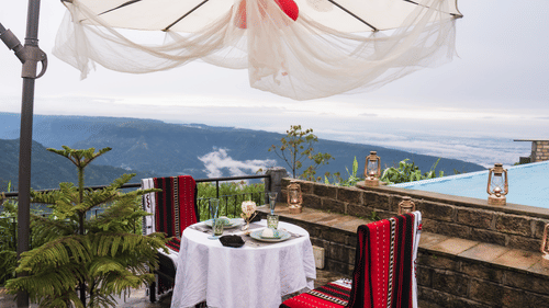 A dining table with two chairs on either side with a view of waterfalls in broad daylight - Polo Cherrapunjee Resort