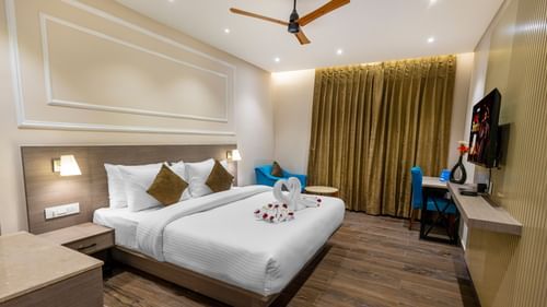 Premium Room at Pride Hotel Rishikesh featuring a plush bed decorated with towels and a TV in front of it mounted on the wall along with a sitting space arranged next to the window