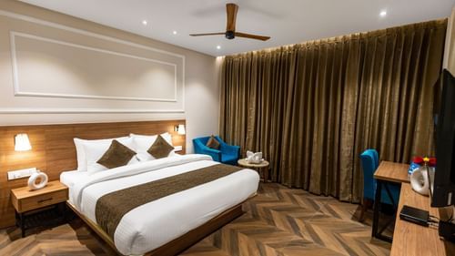 Superior Room at Pride Hotel Rishikesh featuring a plush bed facing the TV mounted on the wall and a sitting space next the window covered by curtains