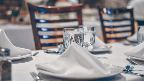 A close-up of a neatly set dining table with white tablecloth, a folded white napkin, a wine glass, and cutlery.