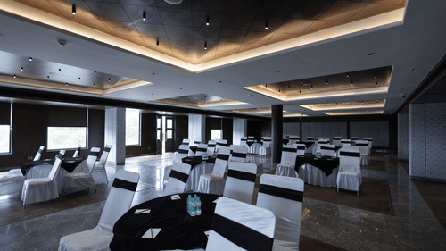 A well-lit banquet hall at Pride Resort, Jodhpur, with tables and chairs dressed in white covers and black tablecloths.