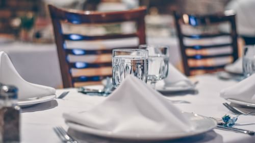 Dining arrangement featuring napkins placed on a plate next to the glass and cutlery