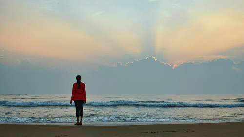 a person standing at a beach looking at the sky after the sunset