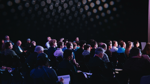 A dim-lit conference hall with people attending a symposium