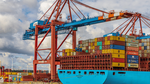 a ship getting containers onto it from the crane next to the ship in a port