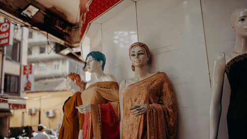 mannequins decked in different sarees in front of a shop with other buildings in the background
