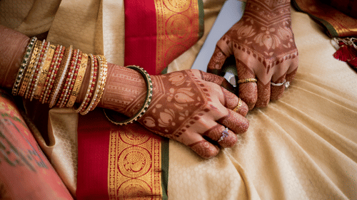 a close up shot of a bride wearing a wedding saree while decked with bangles and mehendi on her hands