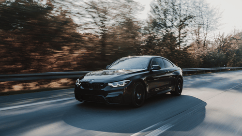 a BMW car travelling on a road with trees next to it and clear sky in the background