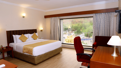 Bedroom with a large window featuring lush green hill views along with a work station in the room at Raj Park Hotel, Tiupati.