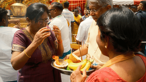 People are gathered around a food stall or offering table during a ceremony.