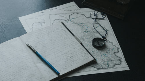 Open notebook with hand-drawn maps and a pen laid out on a desk.