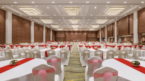 A large banquet hall set up with numerous round tables, white tablecloths, and red runners at Royal Tulip, Kathmandu.