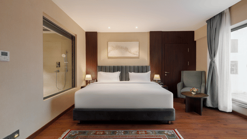 A comfortable bedroom at Royal Tulip, Kathmandu, with a large bed, seating, and a bathroom visible through glass.
