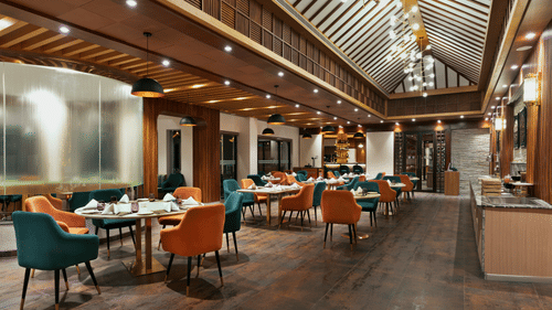 Guras Restaurant dining area at Royal Tulip Shivapuri National Park - Kathmandu with teal and orange chairs, wooden floors, and high ceilings.