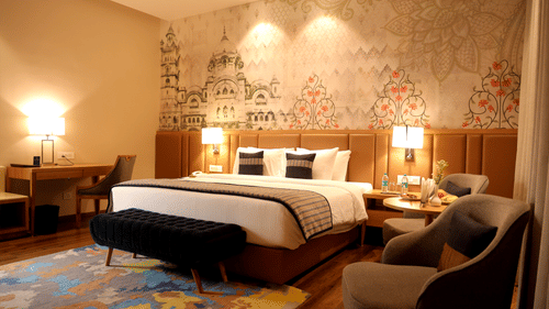 Guest room at Sarovar Portico, Somnath with two beds, lamps, patterned wall design, and seating area.