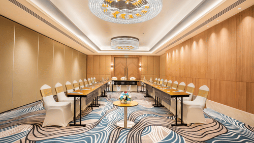 A conference room at Sarovar Premiere Alwar with round tables and chairs arranged on a patterned carpet floor.