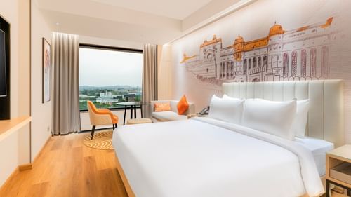 A room at Sarovar Premiere Alwar with a bed, a window with a view, and a wall mural of a building.