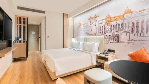 A hotel room at Sarovar Premiere Alwar with a bed, a television, a small table, and a mural on the wall.