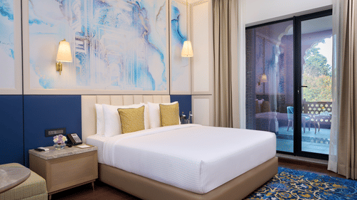 An image of a hotel room in Amritsar with a large bed placed by the side of a balcony with a floor-to-ceiling window parting them - Sarovar Premiere Amritsar