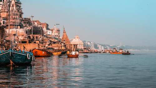 A wide shot of a waterfront with fishing boats docked in the foreground and city buildings in the distance.