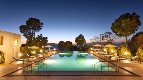 Image of a large swimming pool at Suryavilas in the evening as the premises are surrounded by trees