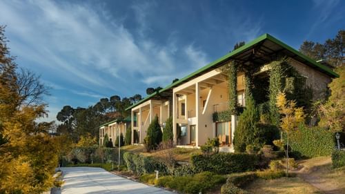 Facade of Suryavilas Luxury Resort and Spa in Solan with a paved driveway and green climbing plants on its exterior walls, under a blue sky with clouds