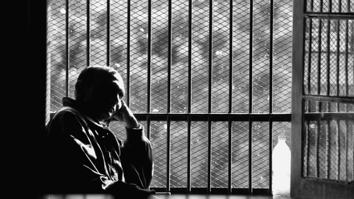 a old man sitting in front of a window looking away with the picture in black and white