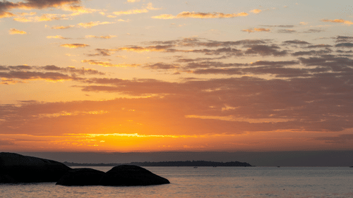 A dramatic sunset over the sea with silhouettes of distant landmasses.
