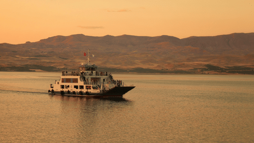 A boat navigates a large body of water during a beautiful sunset.