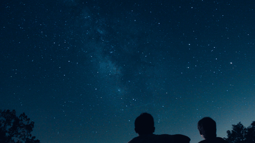 two people sitting and looking at the sky while stargazing