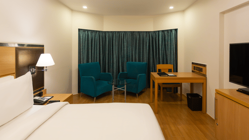 Superior Panoramic Rooms at The Residency Chennai featuring a plush bed with fresh linen facing the TV on a counter beside which is a work desk and a sitting space by the window
